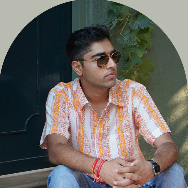 Man in orange and white patterned organic cotton shirt by Dhonk Craft, sitting outdoors