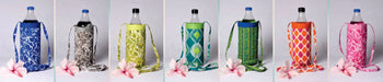 Handcrafted fabric bottle covers in colorful patterns with straps, displayed with pink flowers
