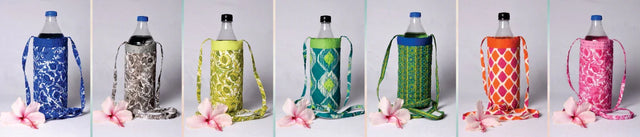 Handcrafted fabric bottle covers in colorful patterns with straps, displayed with pink flowers