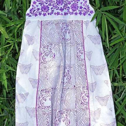 Handcrafted white cotton dress with purple floral, tiger, and butterfly prints, hanging on greenery