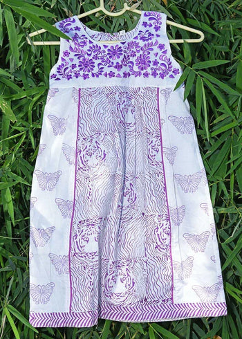 Handcrafted white cotton dress with purple floral, tiger, and butterfly prints, hanging on greenery