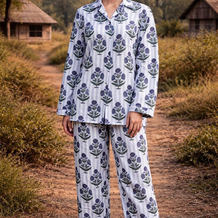 Woman in organic cotton floral pajama set by Dhonk Craft, outdoors near rustic huts.