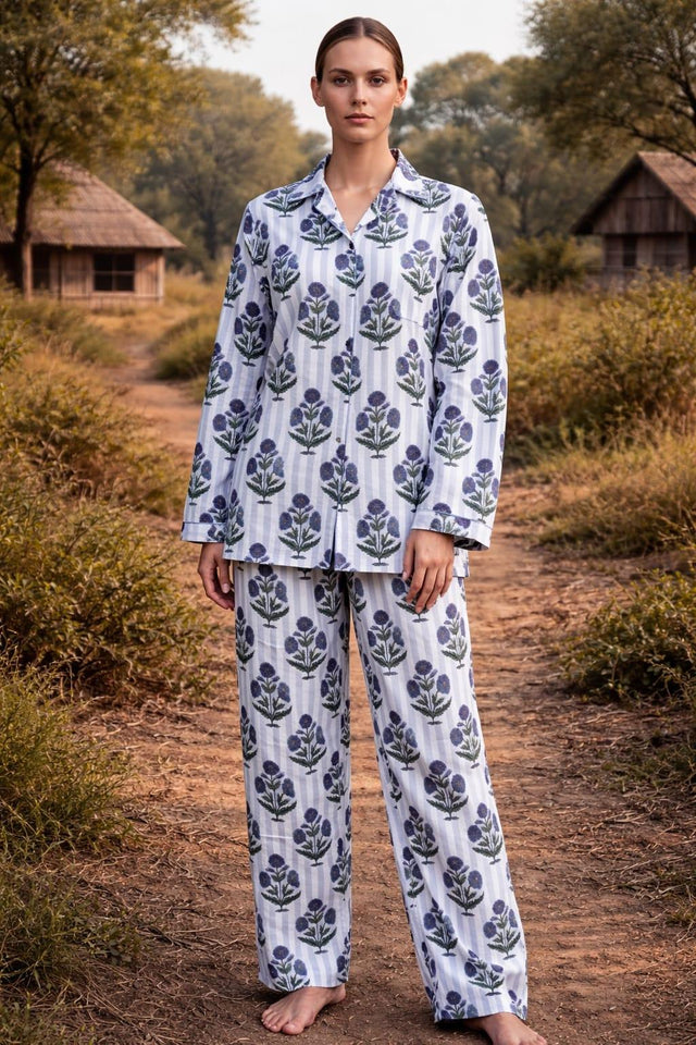 Woman in organic cotton floral pajama set by Dhonk Craft, outdoors near rustic huts.