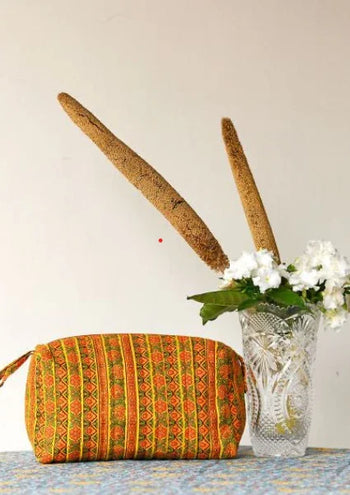 Handcrafted orange patterned purse by Dhonk Craft beside flowers in a glass vase on a table.