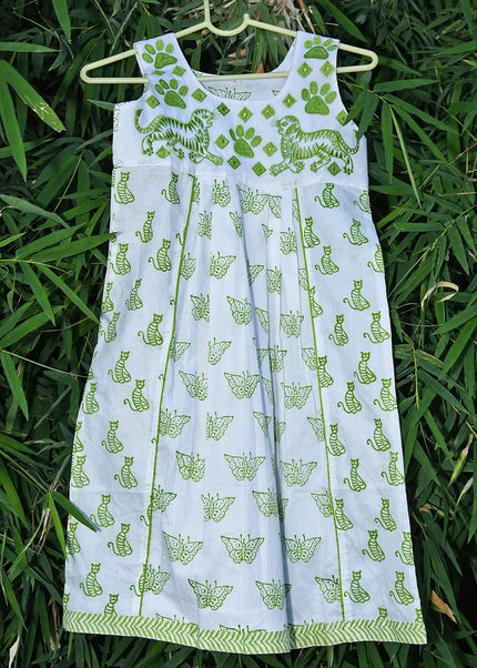 A sleeveless frock with block print animal patterns, displayed on a hanger against a green leafy background.