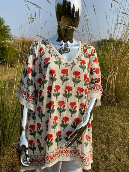 A mannequin wearing a beige Kaftan with a floral pattern displayed in a natural setting with tall grasses.