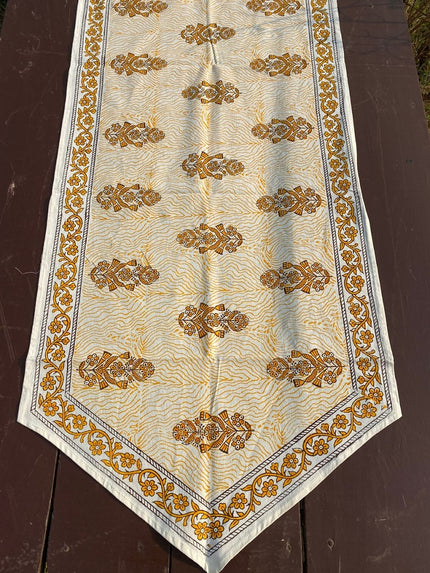 A cotton hand block print table runner with geometric and floral patterns in gold and white colors on a light background, displayed on a wooden surface.