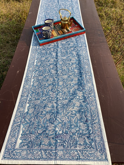 A blue and white floral patterned table runner displayed on a wooden table with a decorative tray and accessories on top.
