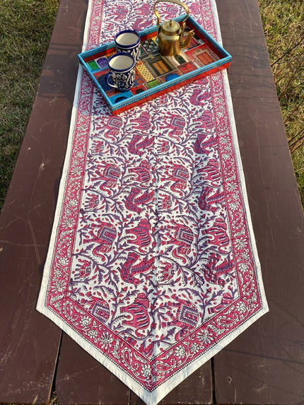 Hand block printed cotton table runner with pink elephant motifs and floral border on a wooden dining table - Dhonk Crafts Amer Collection.