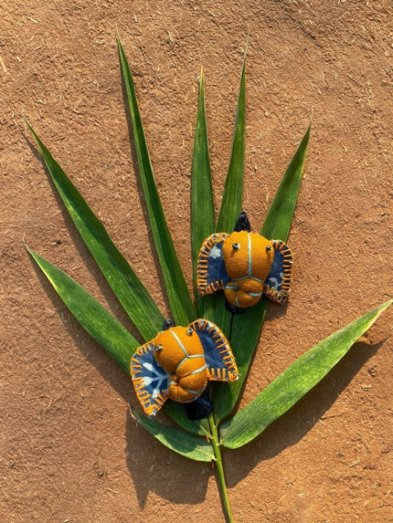 Two hair clips with a floral pattern on a brown background, positioned on a green leaf.