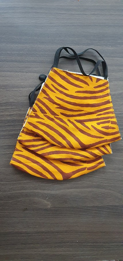 A hand block printed yellow and red striped cotton mask laid flat on a wooden surface.