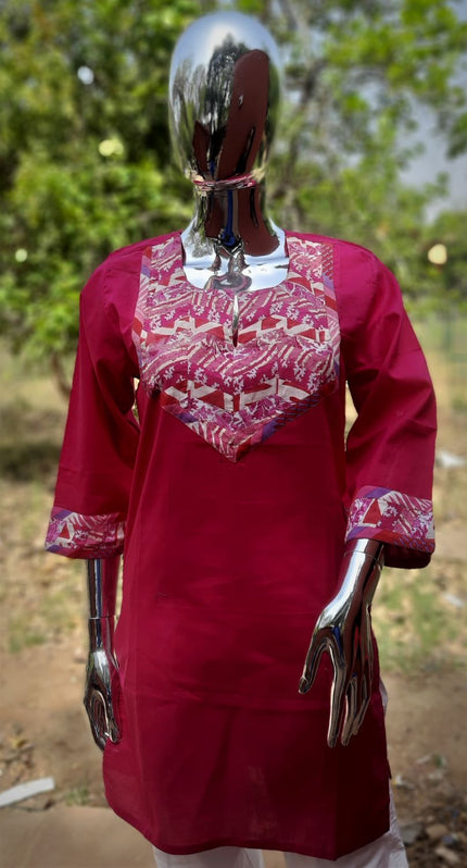 A mannequin displaying a red patch work tunic with detailed embroidery on the sleeves and neckline.