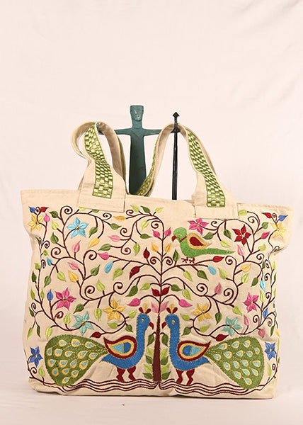A multicolored floral and peacock embroidered tote bag with green straps and a black handle.